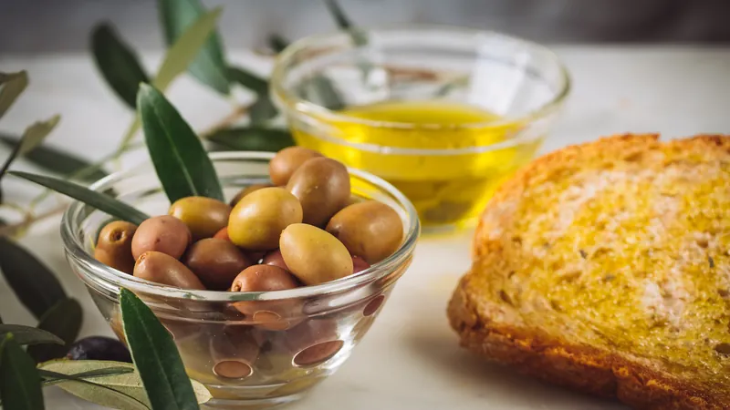 Geröstetes Brot, eine Schale Oliven und Olivenöl auf einem Tisch