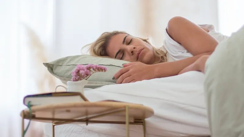 Frau schläft in weißer Bettwäsche, Buch und Blumen daneben